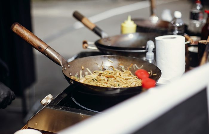 Chef cooking noodles and vegetables in a pan on fire